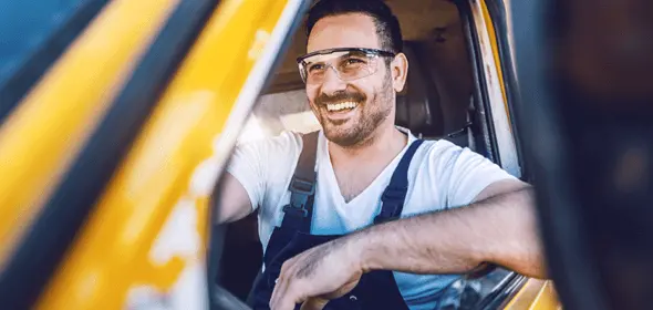 A man wearing work goggles driving a truck and smiling